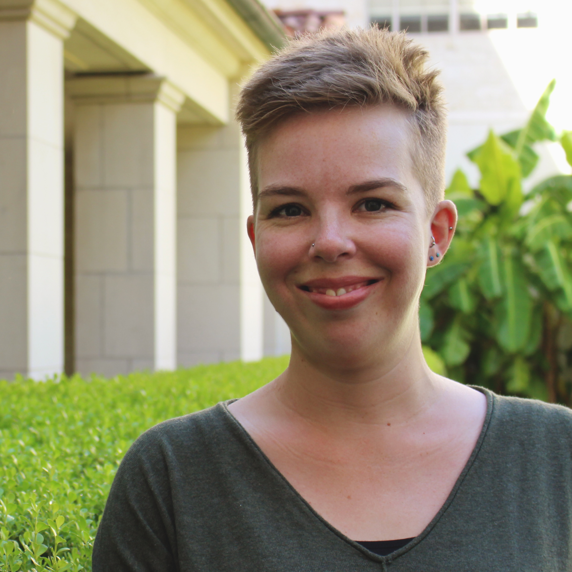 Headshot of Beck Wise, a white woman with short blonde hair standing in front of a sandstone building